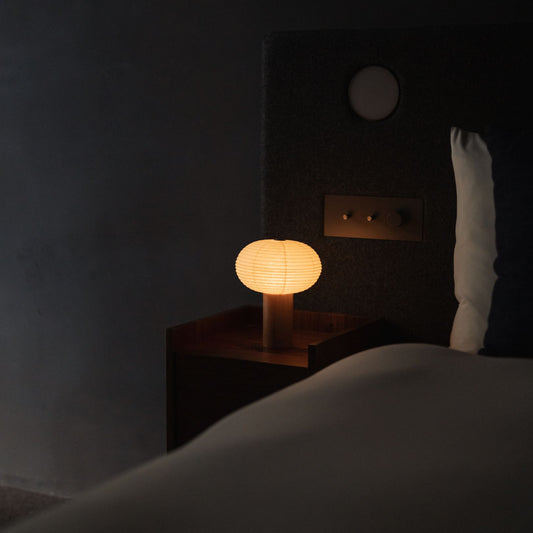 A Japanese paper table lamp "TORCHIN OVAL" on a bedside table.