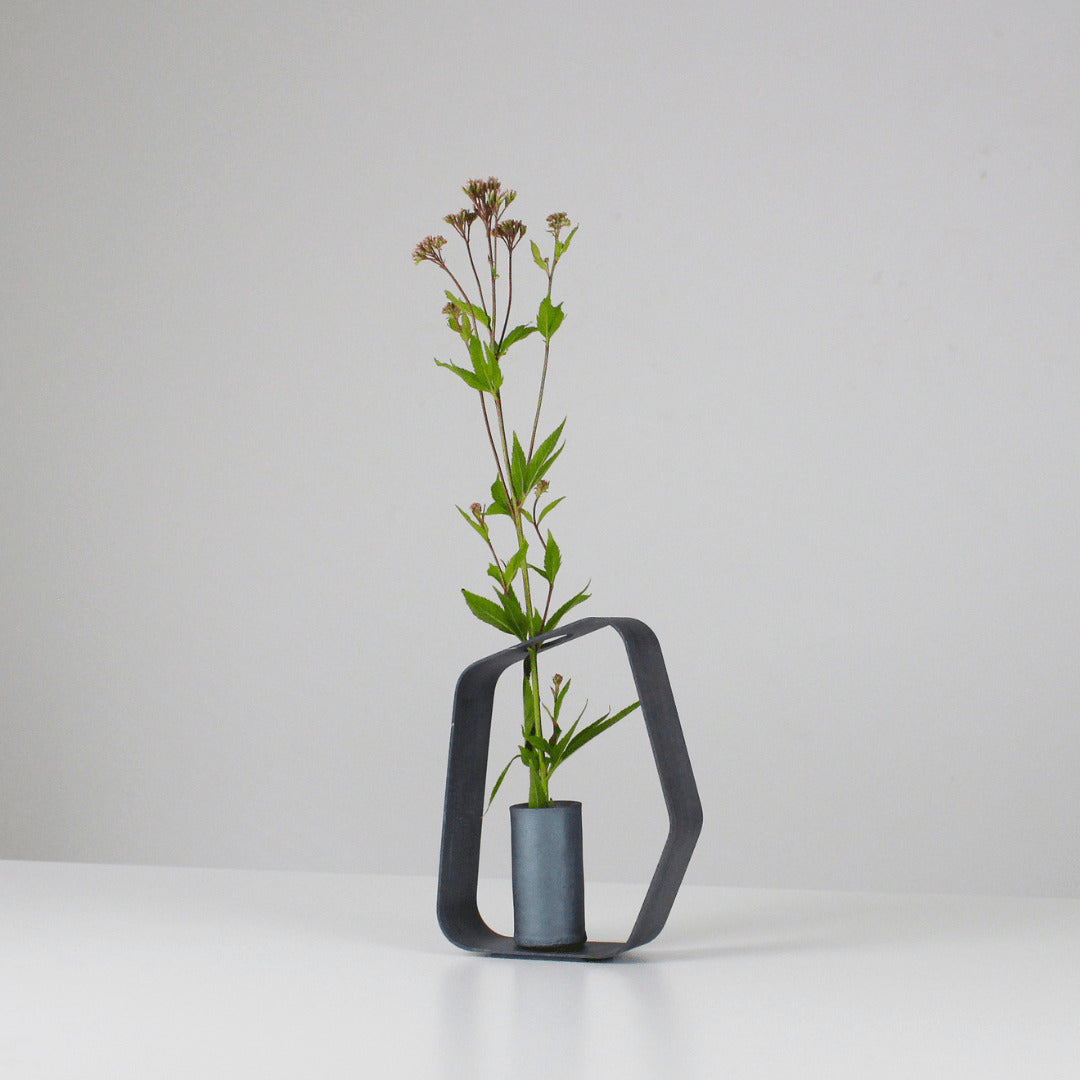A minimalist black iron vase crafted using traditional Japanese roof tile making techniques, paired with a black wood frame.