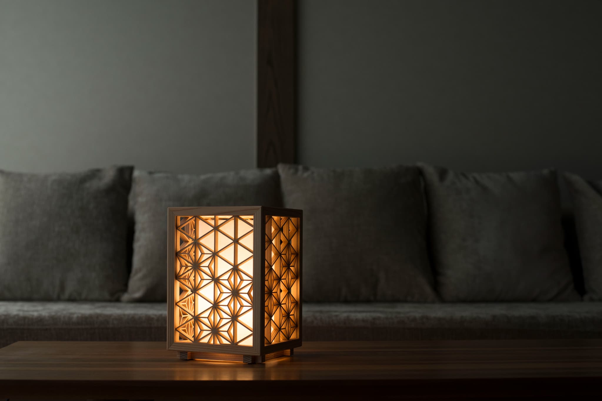 Japanese Kumiko table lamp, meticulously handcrafted with 260 pieces of premium Akita cedar, casting a warm and inviting glow on a table in a Japandi living room.