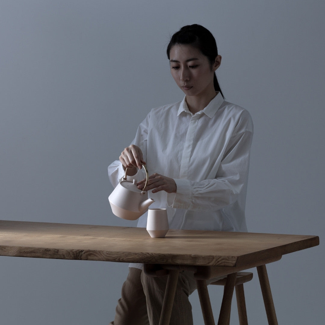 Woman serving Japanese green tea with teapot and yunomi tea cup on wooden table