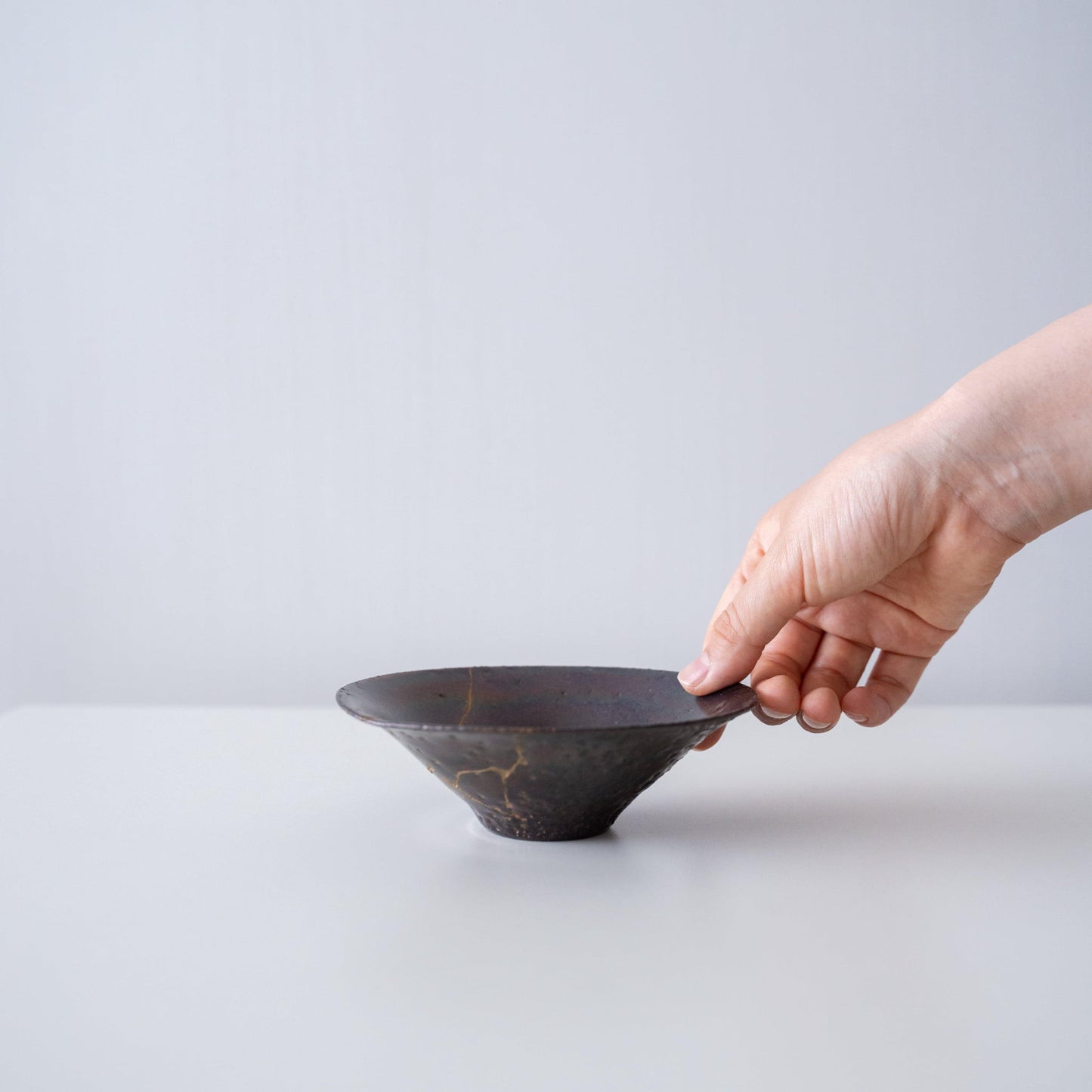 Hand holding a leaf-shaped bowl repaired with Kintsugi, a traditional Japanese technique.