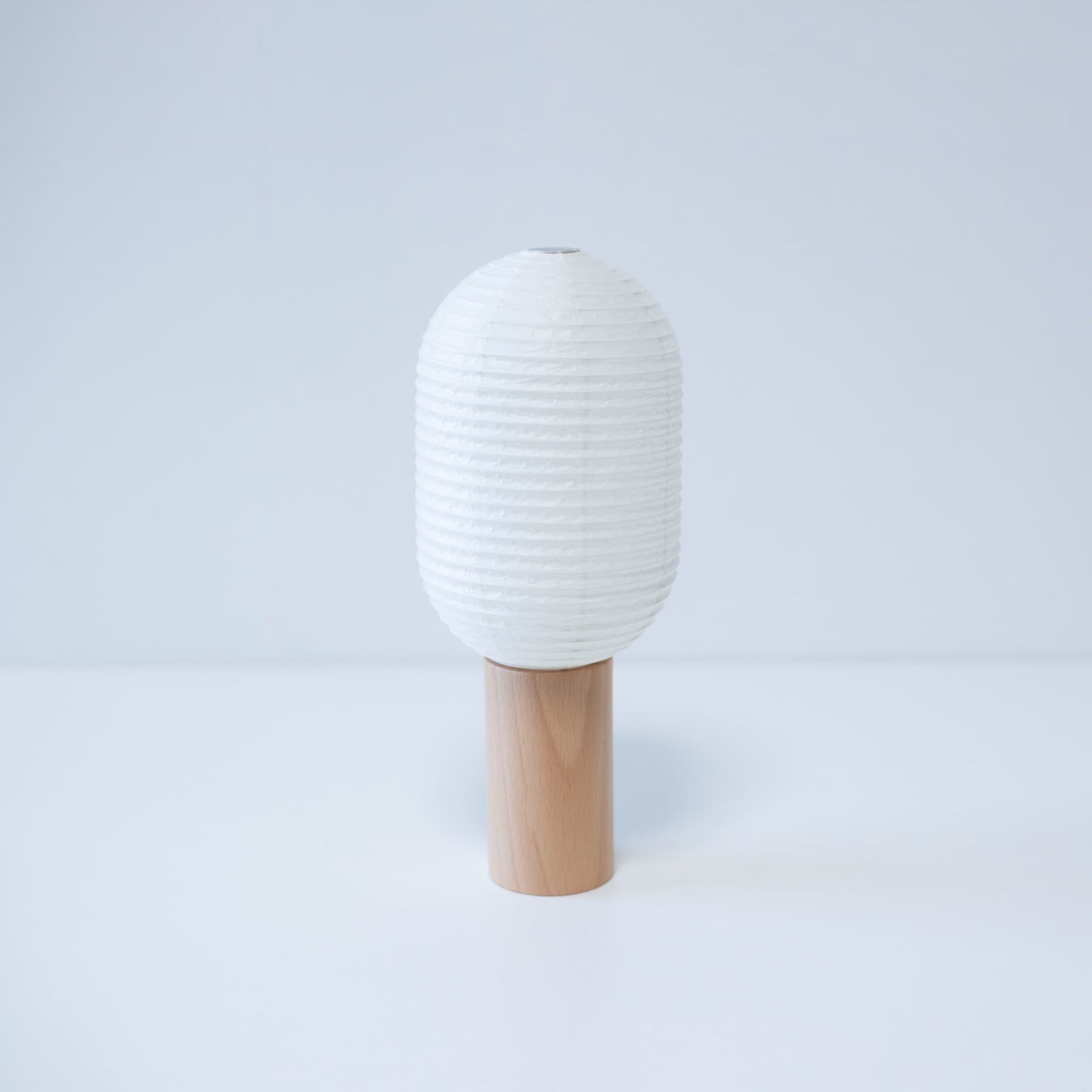 Japanese paper lamp "TORCHIN VERTICAL" featuring a tall, cylindrical white washi paper shade and a wooden handle, handcrafted in Yame, Fukuoka, Japan.