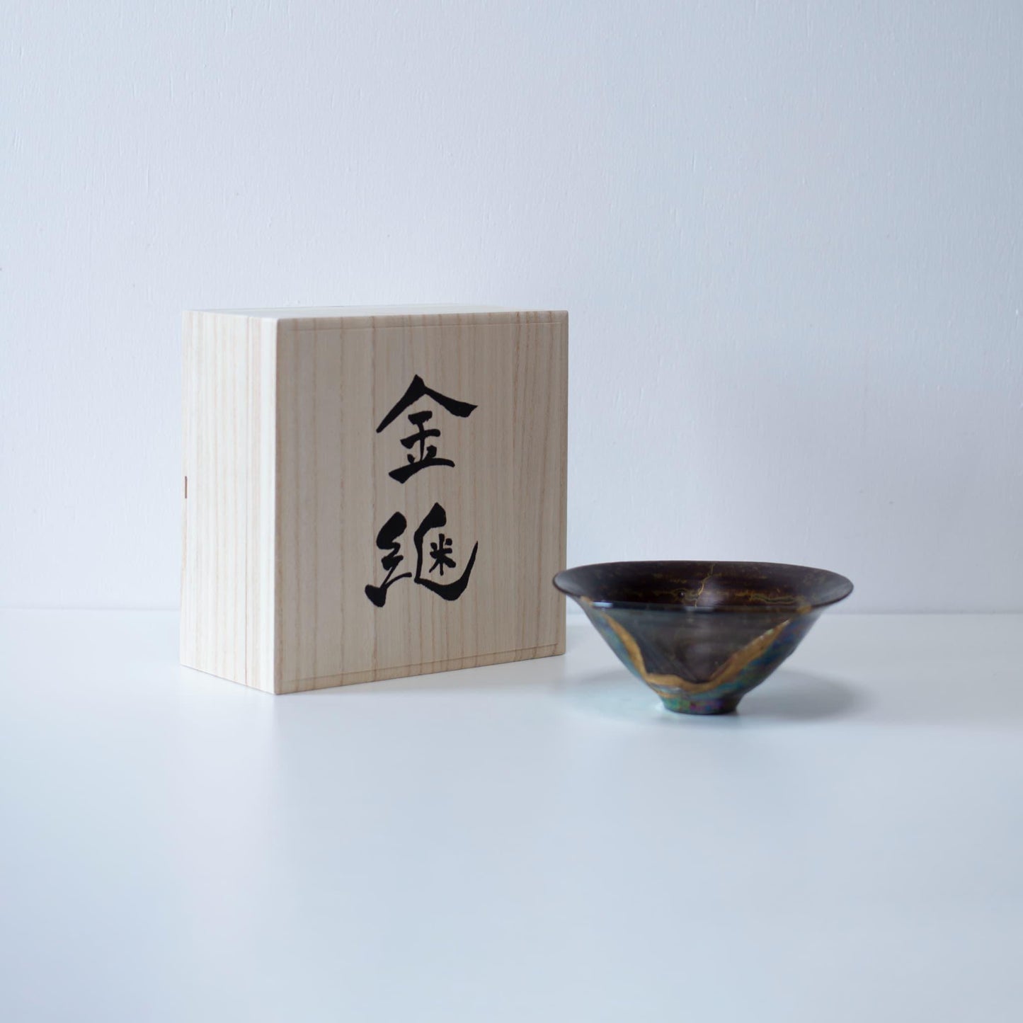 A stunning bowl repaired using the intricate Japanese art of Kintsugi, featuring a glass inlay and presented in a paulownia wood box with a gold inlay inscription.