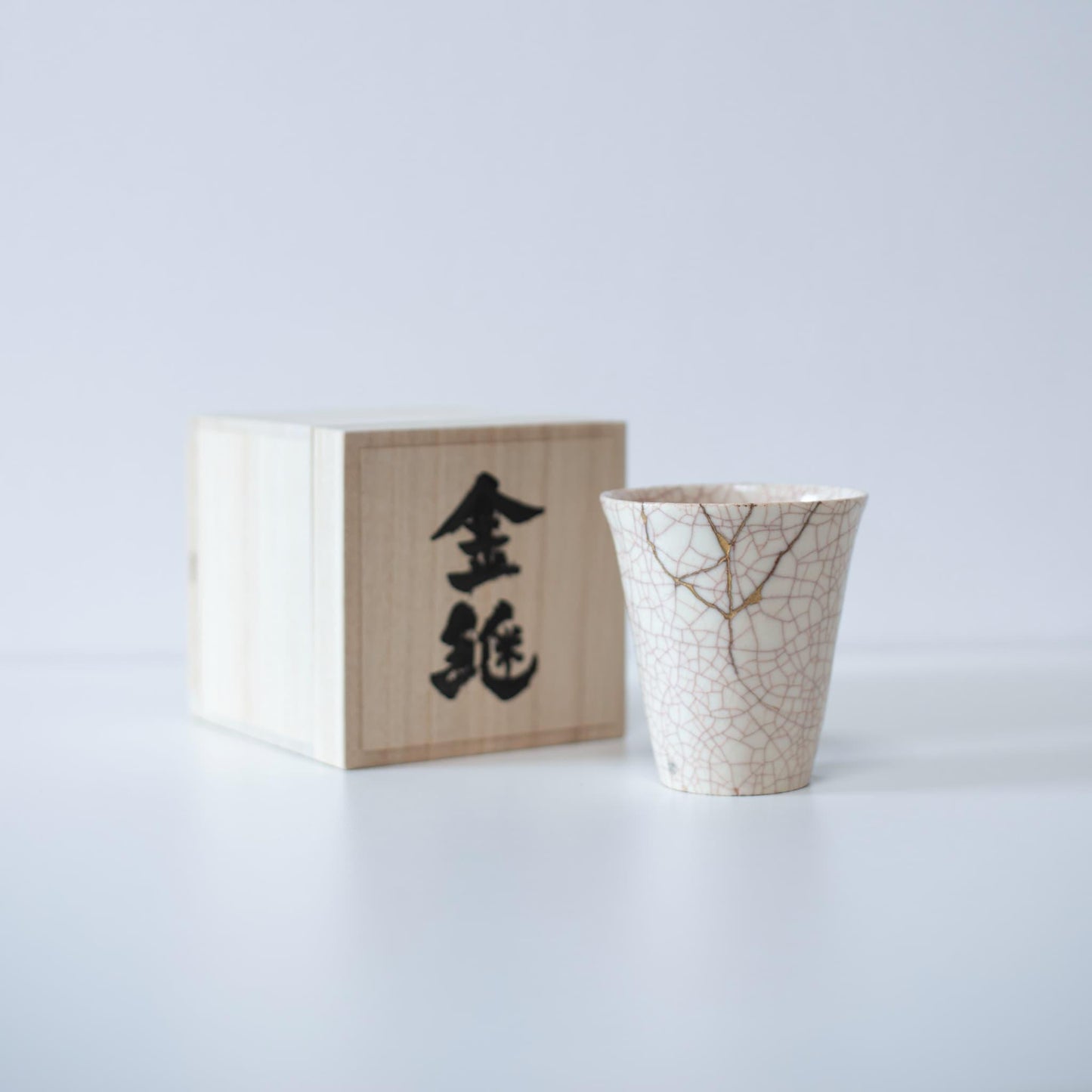 White cup repaired with Kintsugi, a traditional Japanese technique, presented in a paulownia wood box with the inscription "Kintsugi".