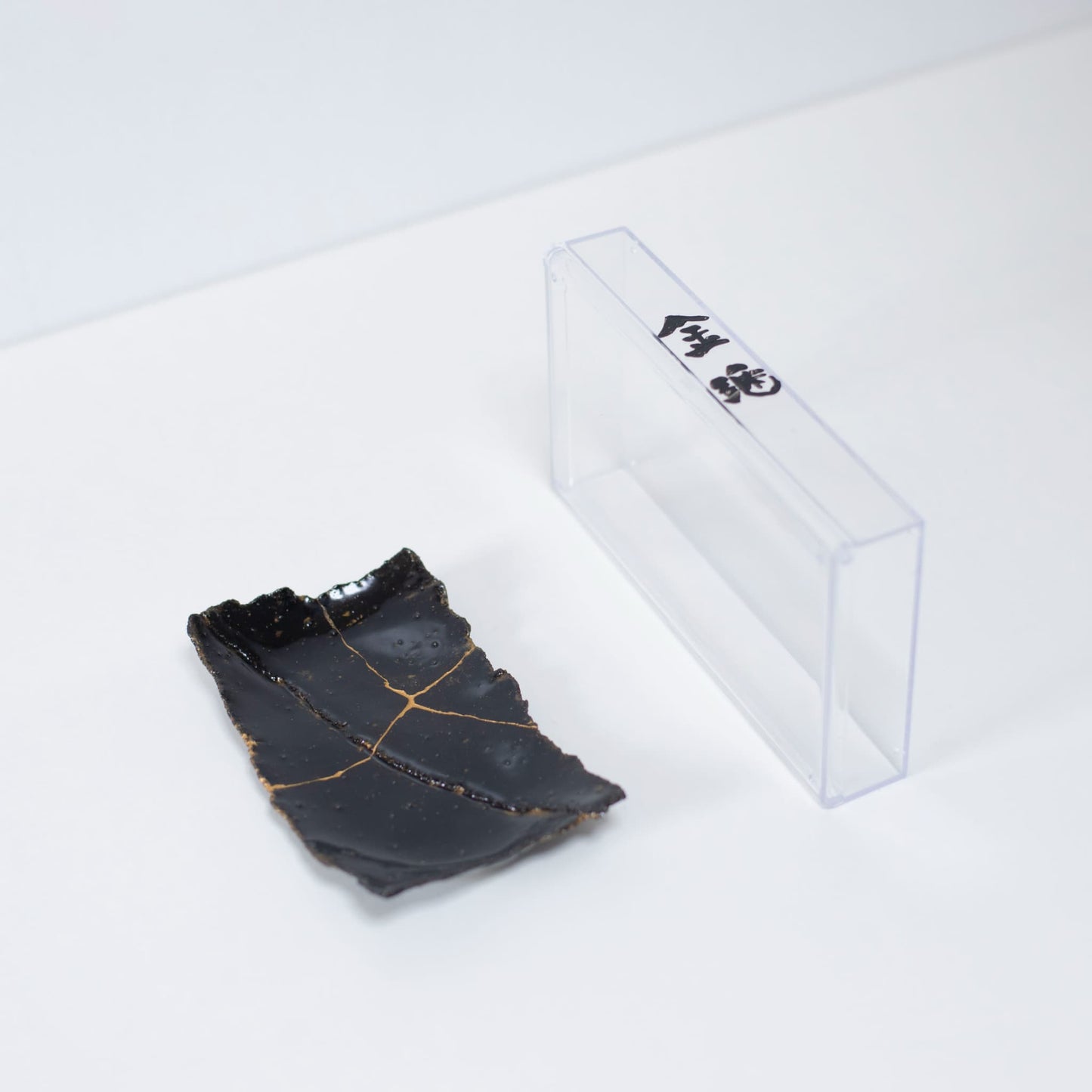 Kintsugi Plate "Tenmoku" Black 01 presented with a clear case, top view.