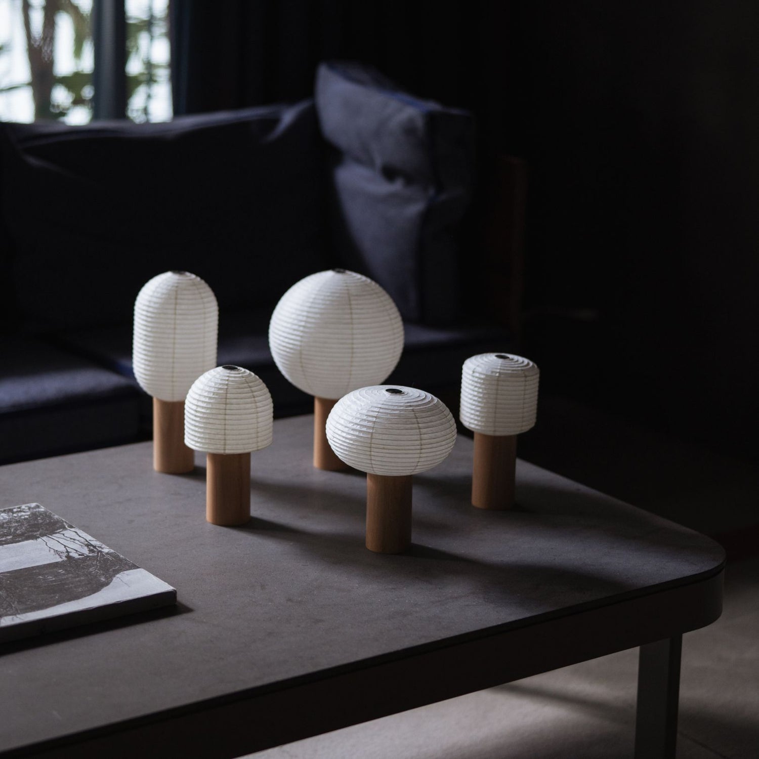 Five different Japanese Paper Table Lamps "TORCHIN" on a gray table in a dimly lit room.