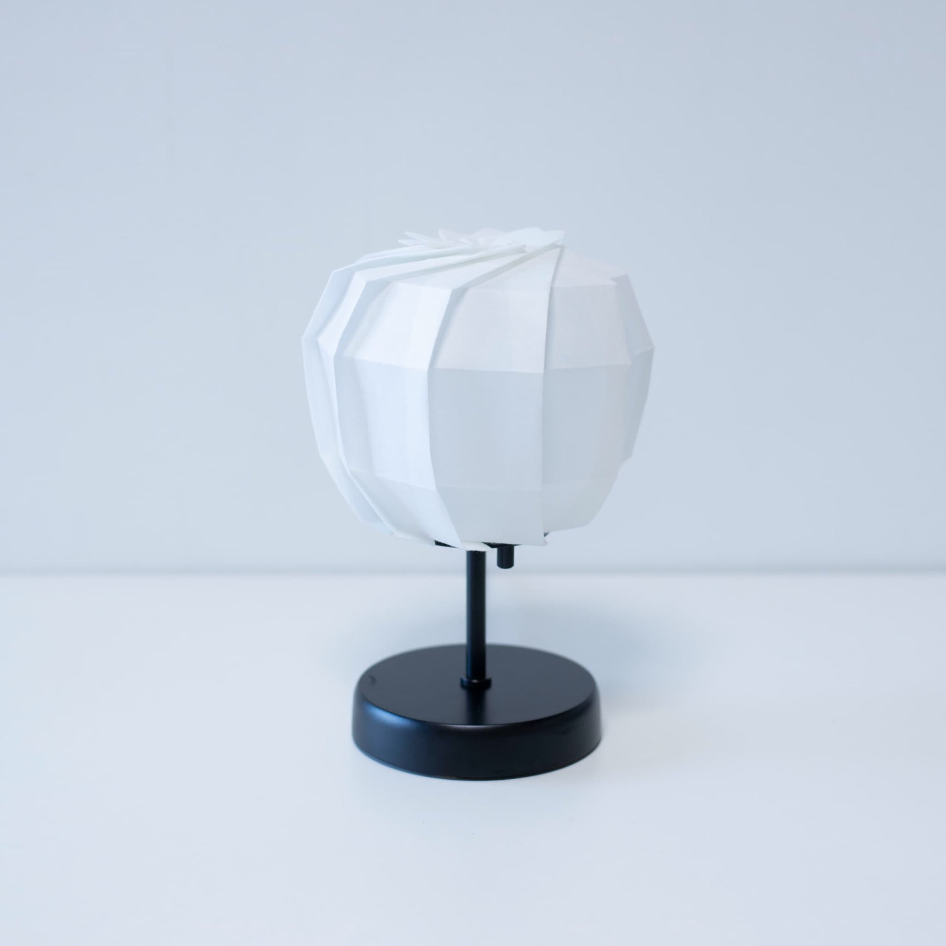 Stylish Origami table lamp featuring a black stand and a spherical white lampshade crafted from intricately folded washi paper.
