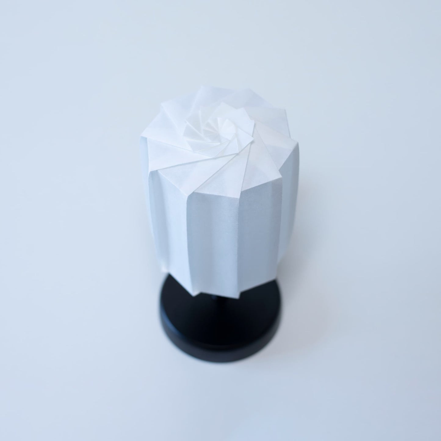 Origami Table lamp "tutu" with a black stand and a white cylindrical lampshade made of pleated washi paper, adding a modern touch to any room.
