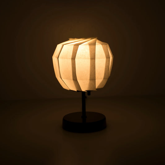 Origami paper table lamp "maru" with a black stand and a spherical white lampshade crafted from intricately folded washi paper, emitting a warm and inviting light.