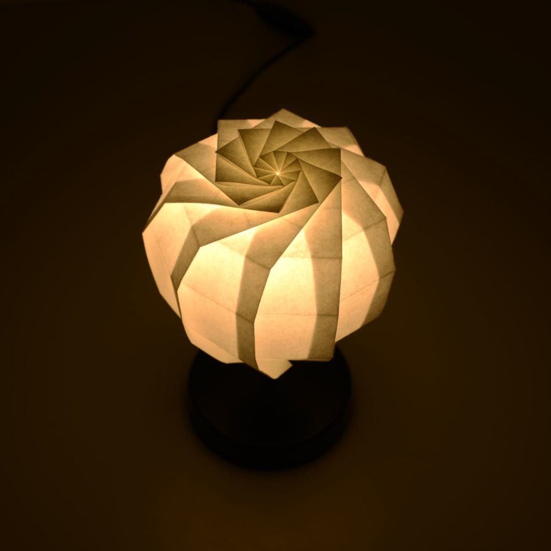 Origami Table lamp "maru" with a black stand and a cylindrical white lampshade made of pleated washi paper, emitting a warm and inviting light.