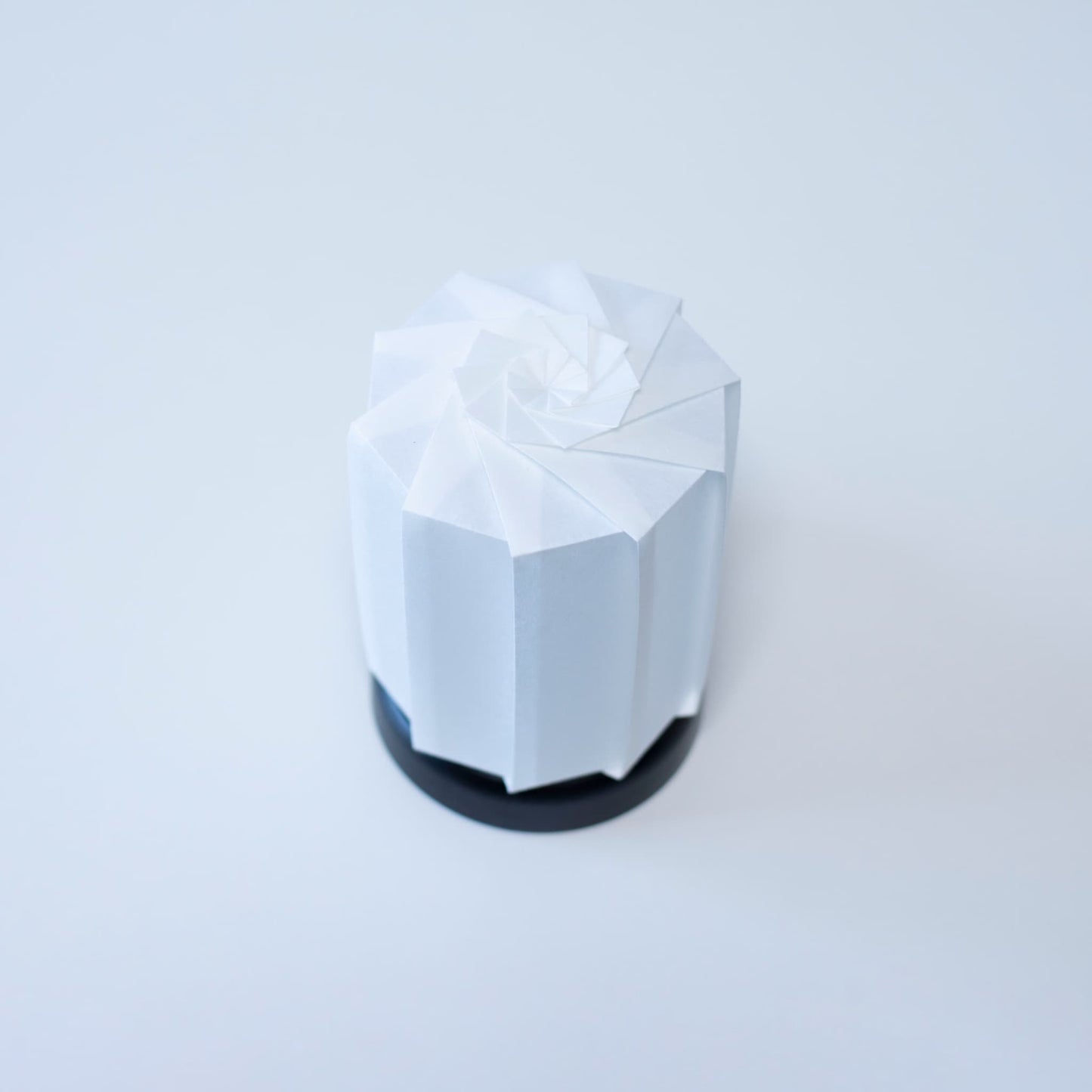 Modern Origami table lamp tutu M" with a black base and a white cylindrical lampshade made of textured washi paper, creating a warm ambiance.