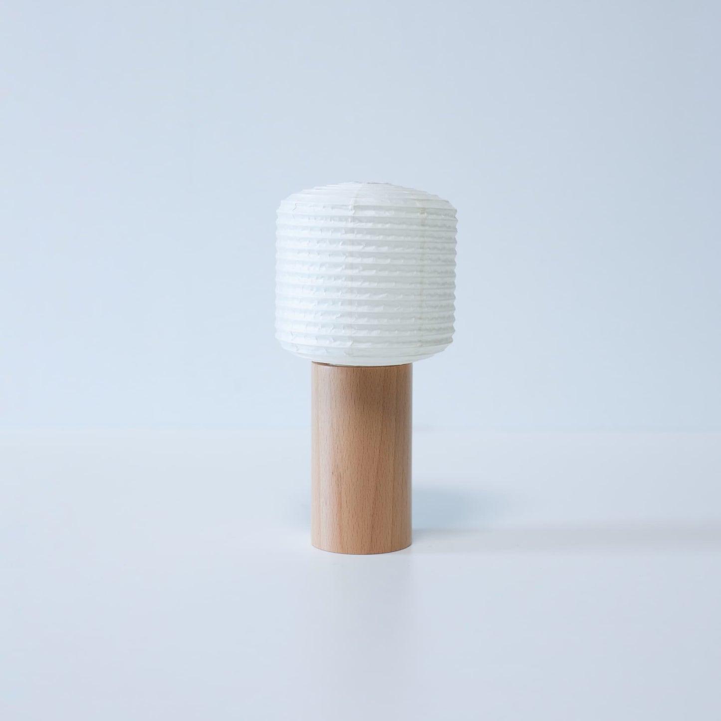 A portable paper lamp with a wooden base and cylindrical paper top against a white background