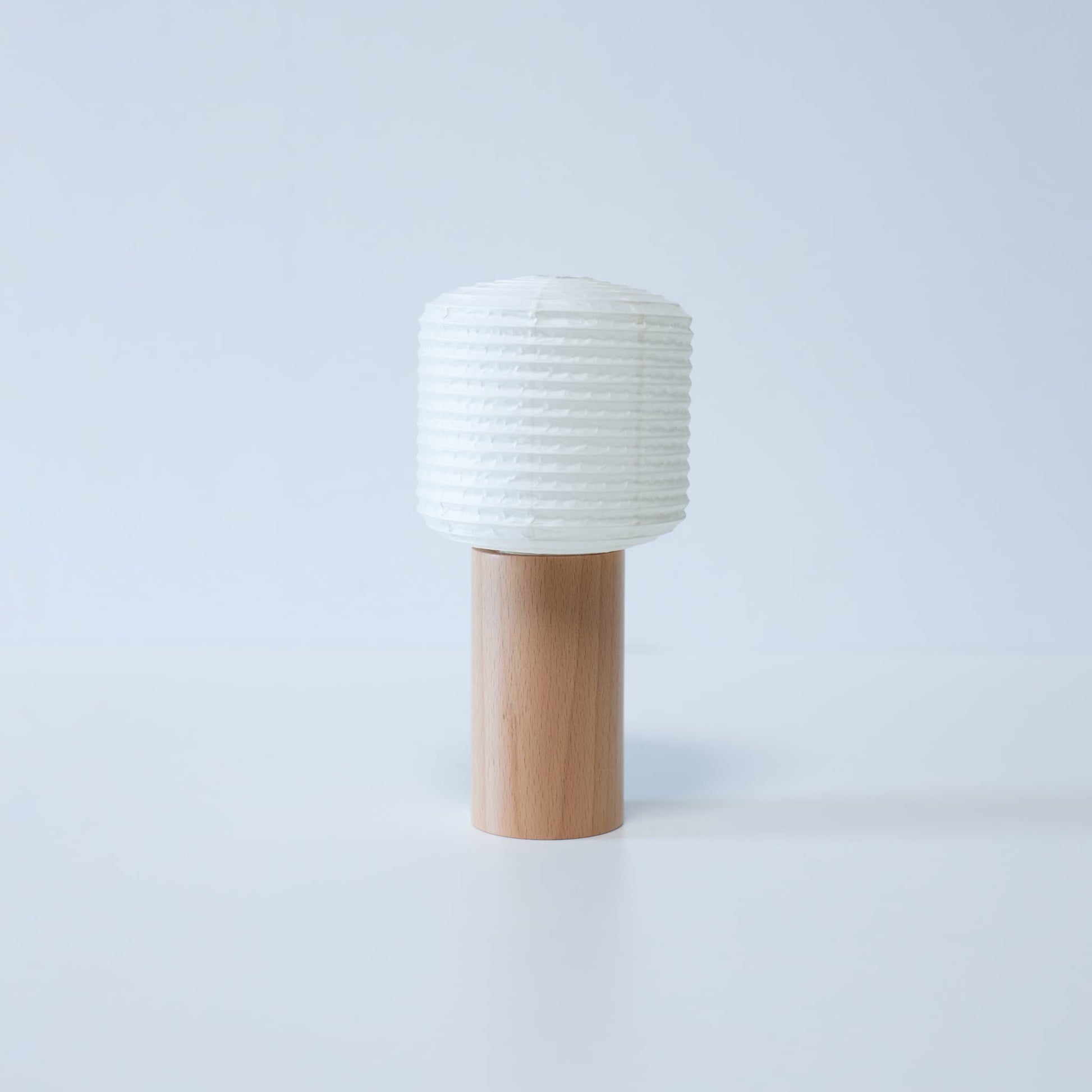 A portable paper lamp with a wooden base and cylindrical paper top against a white background
