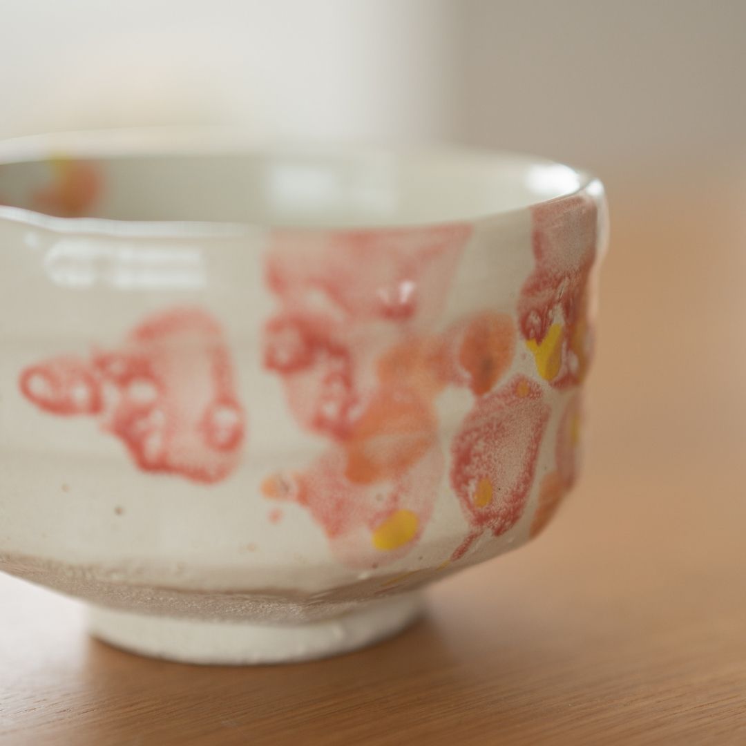 Tæt på detalje af en Shino-keramik matcha-skål, der viser den taktile lertekstur og et unikt rødt og orange glasurmønster skabt ved en traditionel "flicking"-teknik.