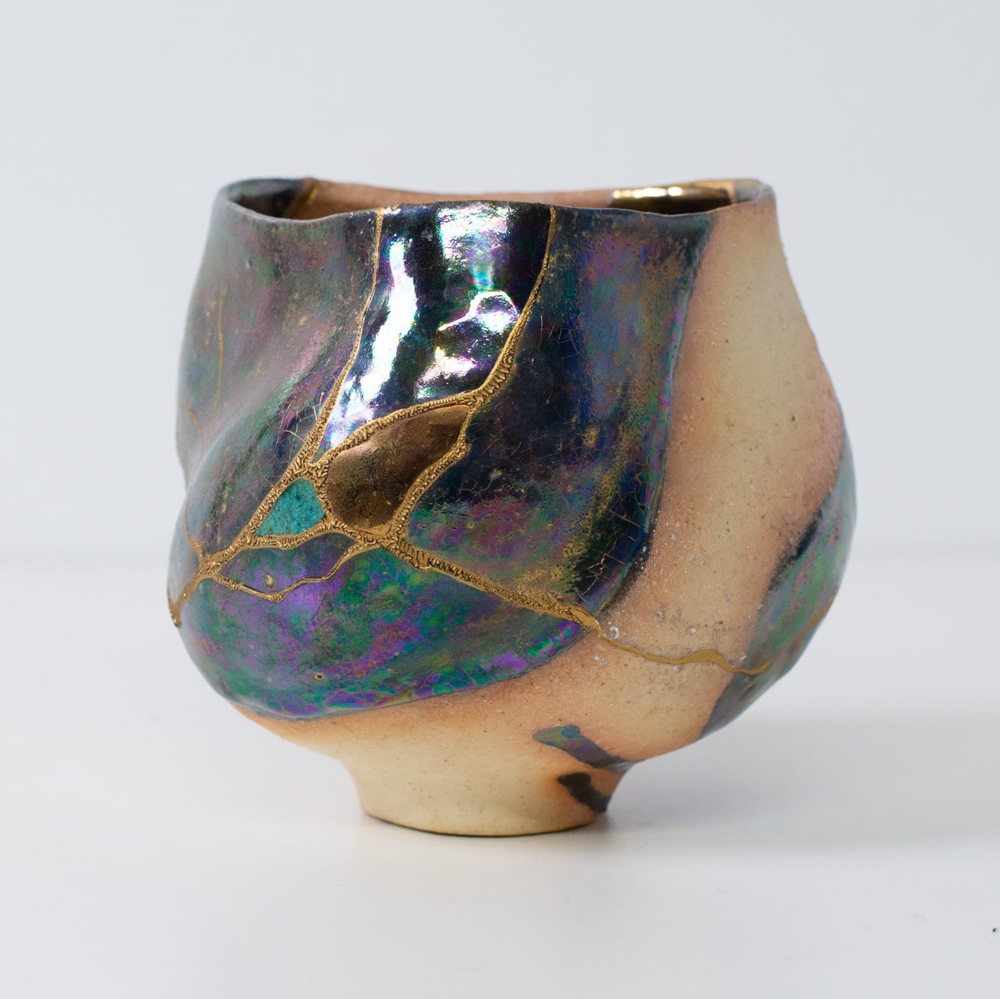 Side view of kintsugi pottery matcha bowl with iridescent glaze and golden restoration