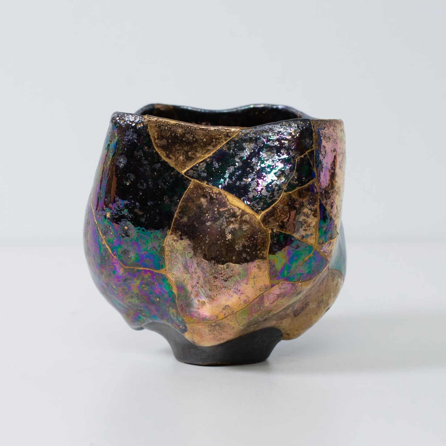 Side view of kintsugi pottery matcha bowl with gold seams and iridescent glaze