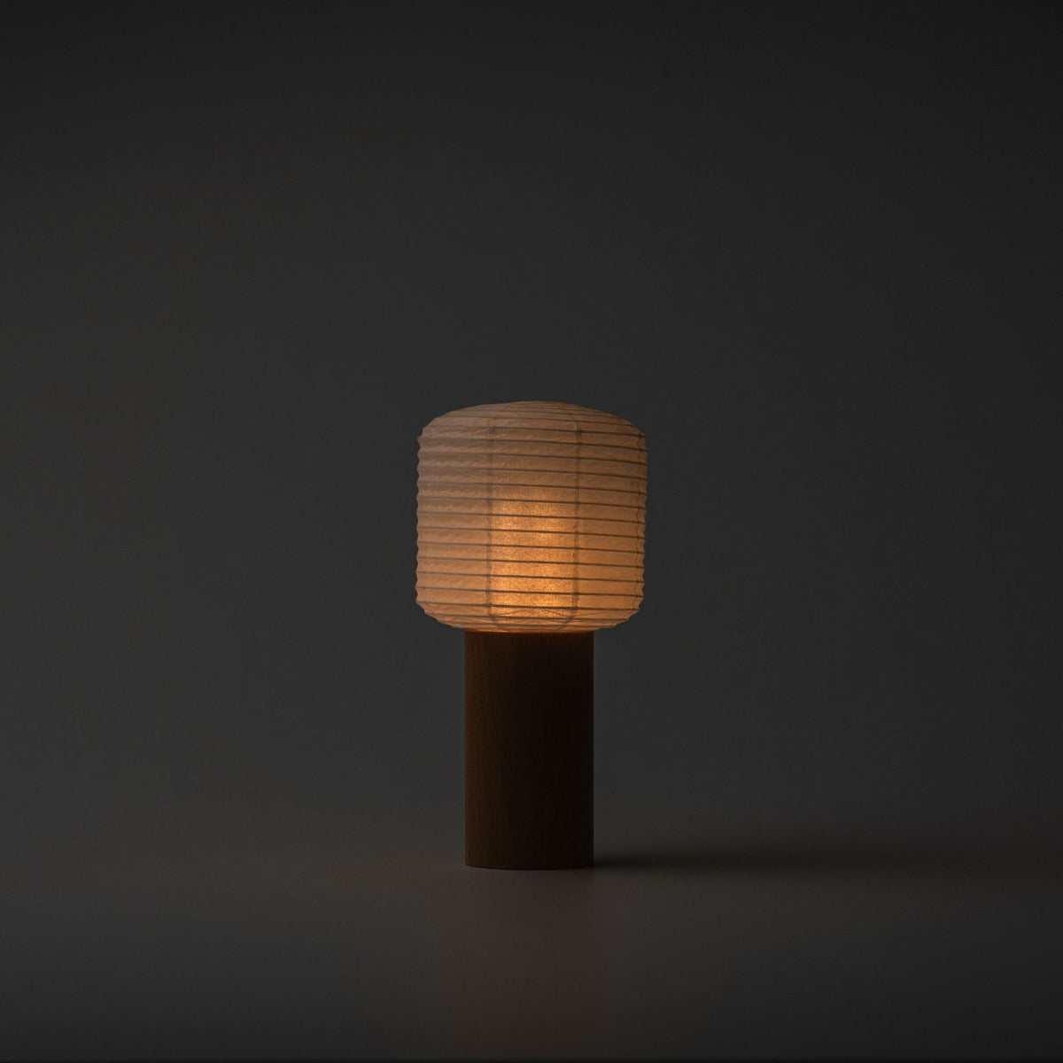 Een draagbare papieren lamp die zacht gloeit met een warm licht in een donkere kamer, met een houten handvat en papieren bovenkant