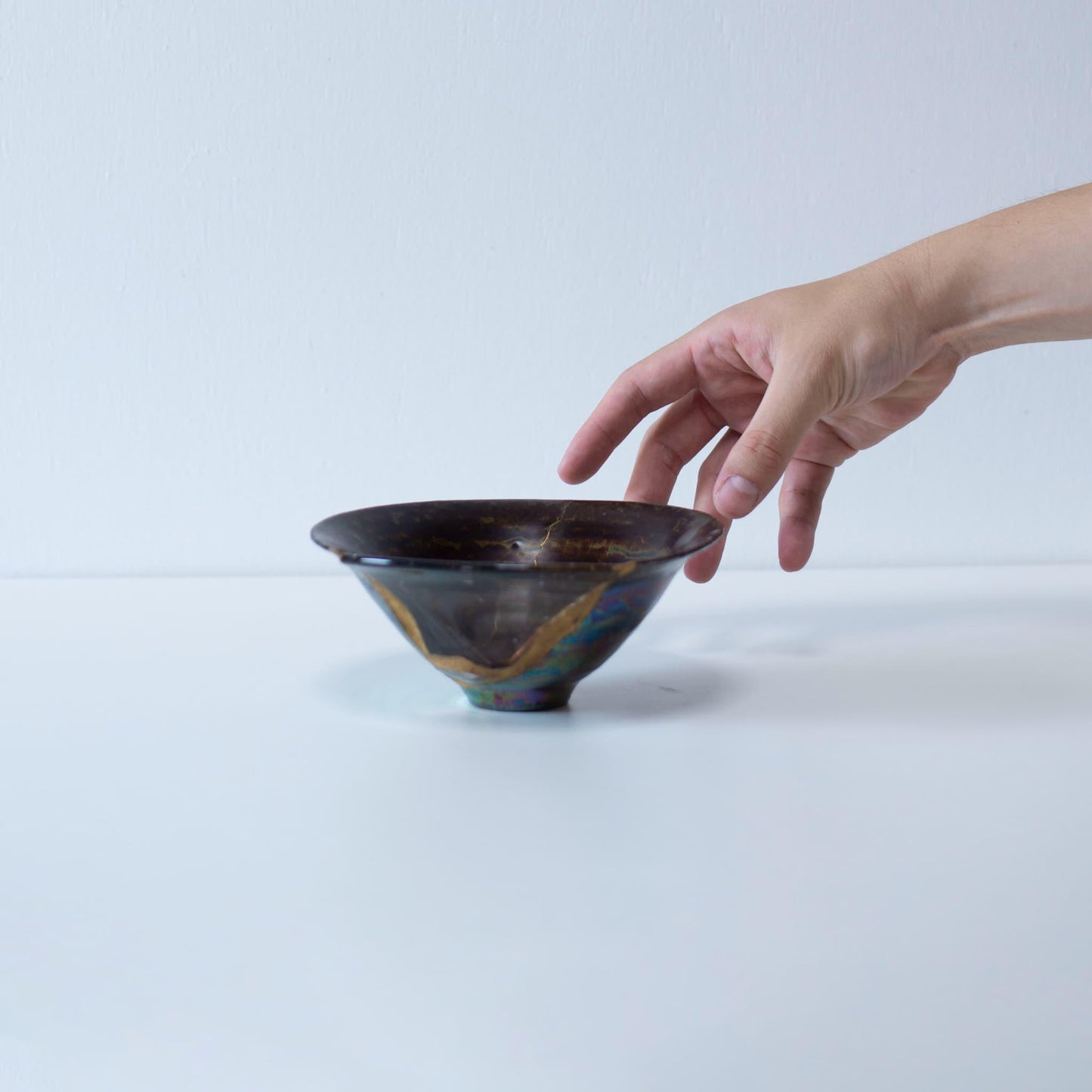 A hand cradling a Kintsugi-repaired bowl, showcasing the intricate gold lines that mend the broken piece.