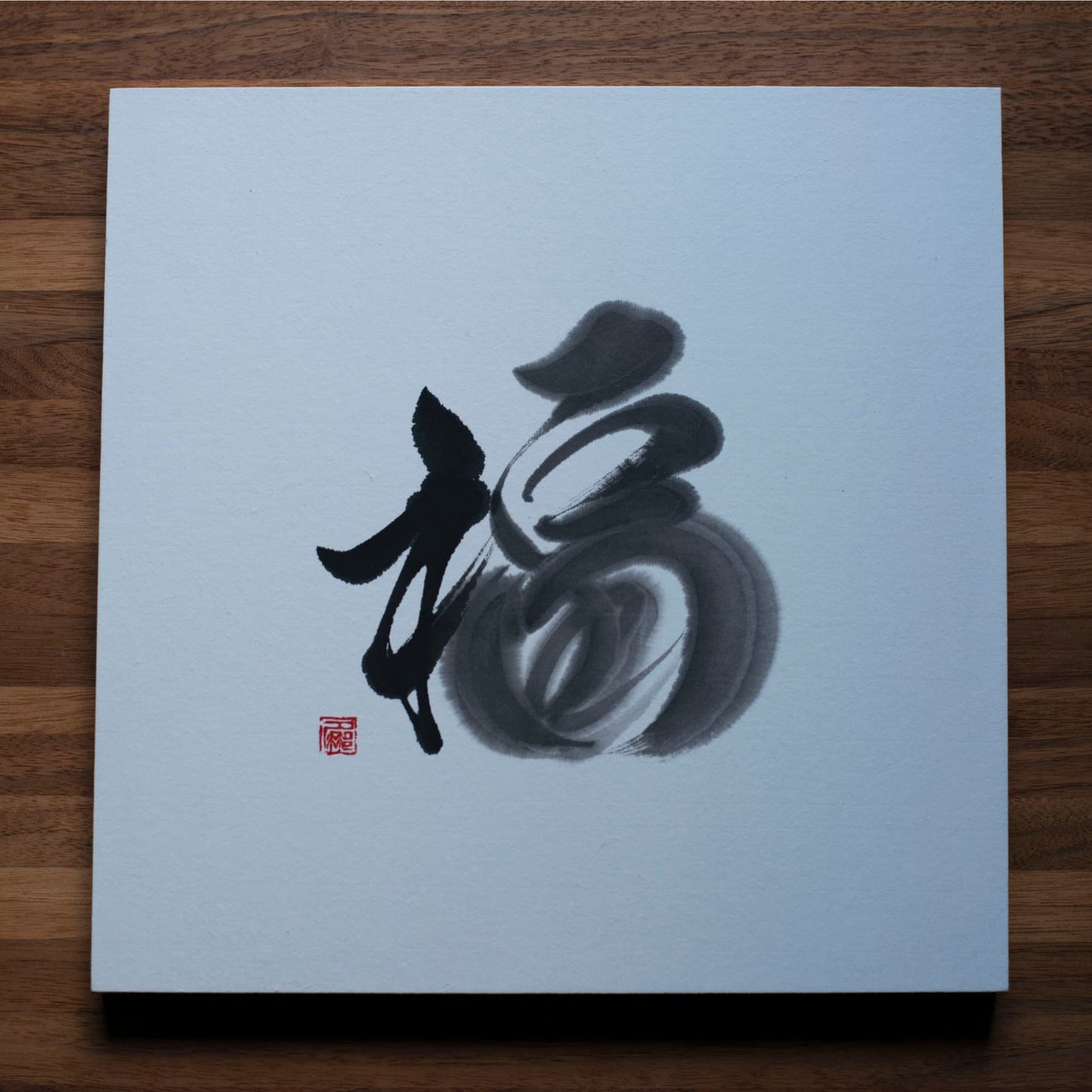 Direct top-down view of a square panel with '福' (fortune) in Japanese calligraphy, placed on a wooden table.