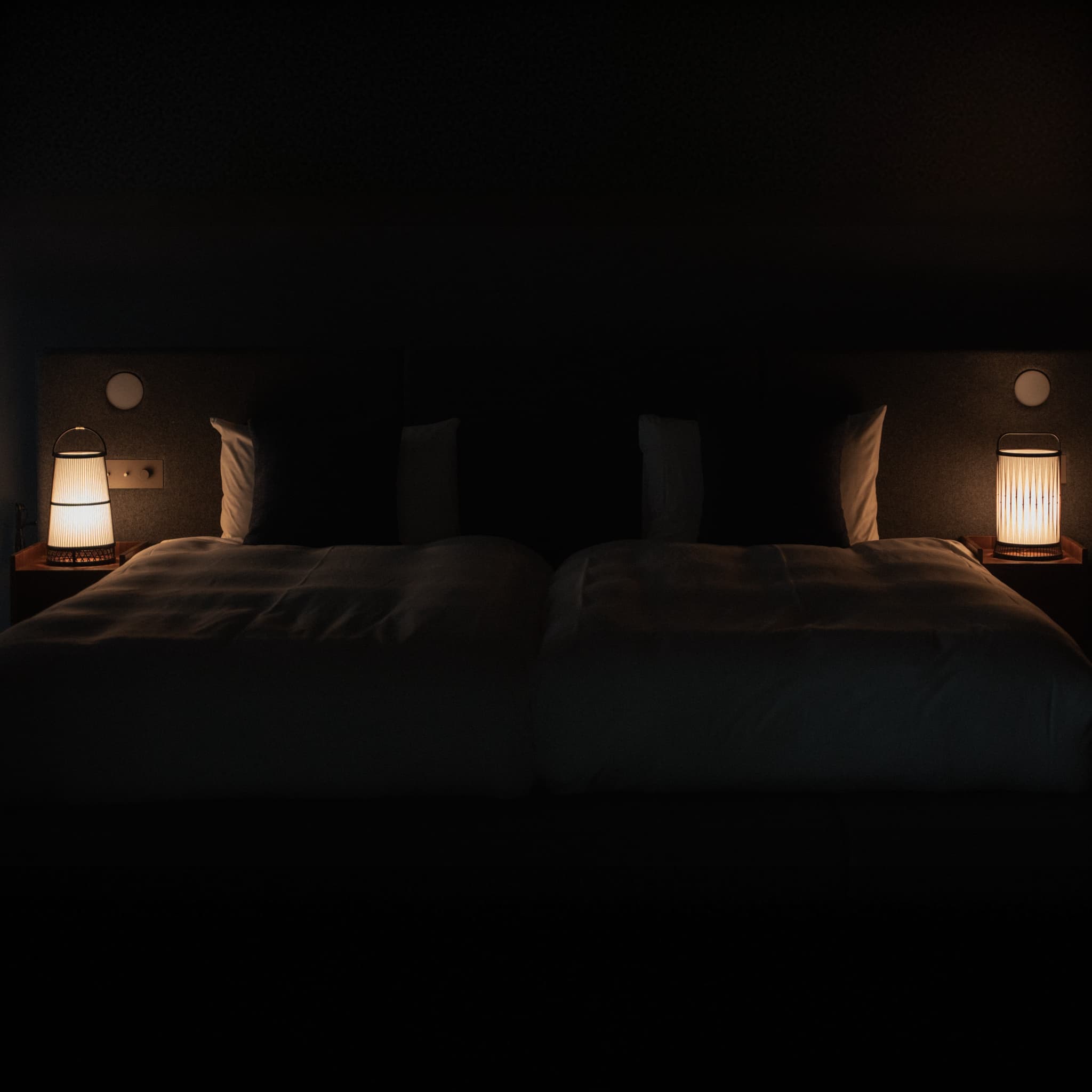 Two traditional Japanese bamboo floor lamps, handcrafted in Shizuoka, illuminate a Japandi-style bedroom.