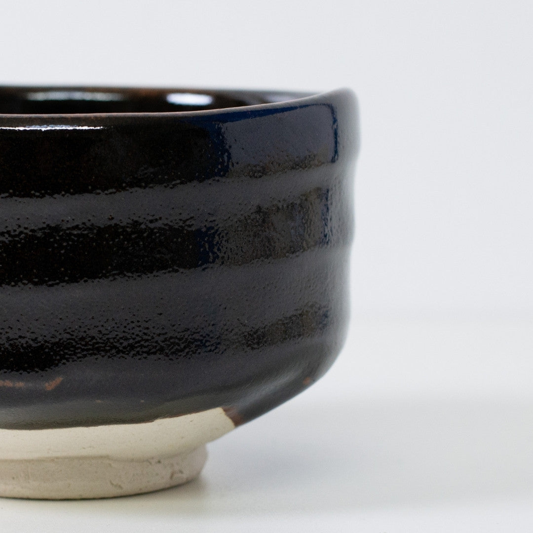 Gros plan sur un bol à matcha noir de type chawan, révélant la texture unique "Yuzu" et la base en argile Shino brute pour une esthétique wabi sabi.