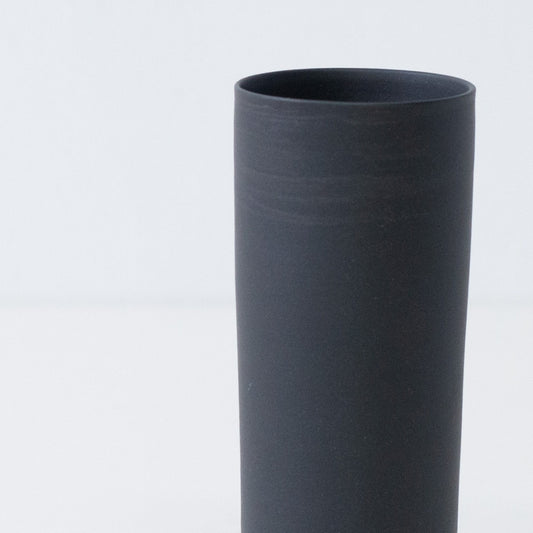 Close up of a textured matte black Japanese flower vase showing handcrafted trowel marks on unglazed stoneware.