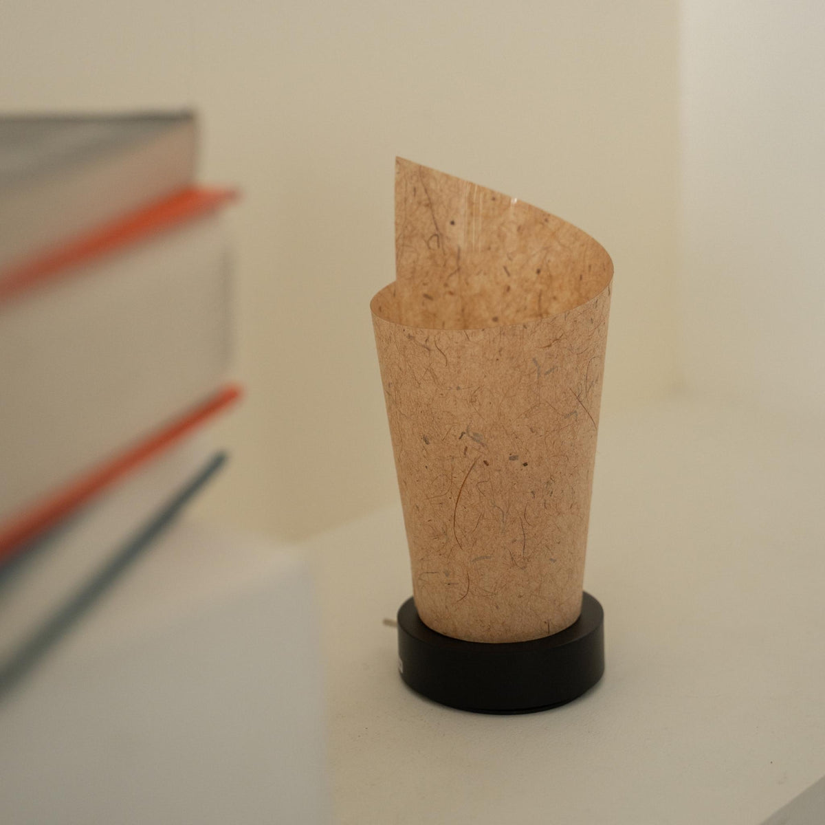 Close-up van een onverlichte Japanse papieren tafellamp "Maki" Cederbast, die het opgerolde ontwerp en de natuurlijke papieren textuur voor wabi-sabi decor laat zien.