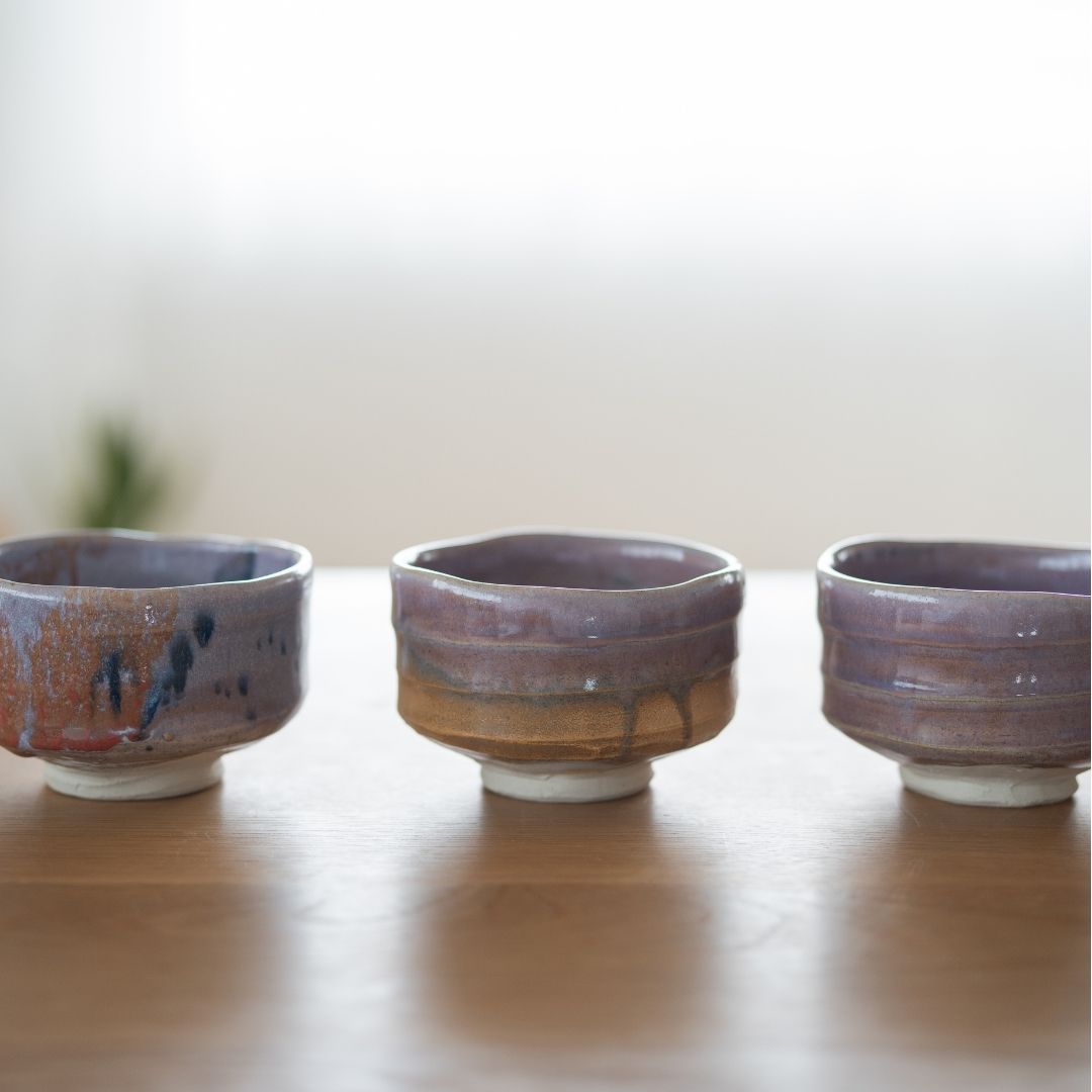 A collection of three handcrafted Japanese matcha bowls from Shinzan Kiln. Navy & Red Splash, Pale Violet Haze, and Pale Violet.