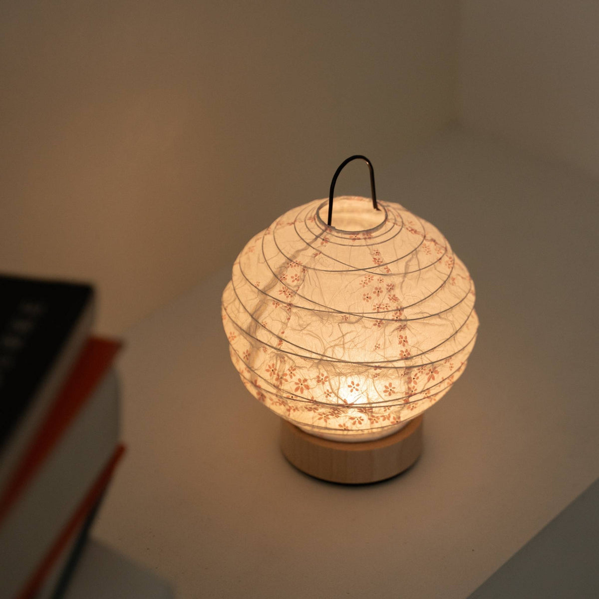 Ronde, gloeiende Japanse papieren tafellamp "Yuhi" Sakura, die dient als een gezellige accentlamp naast boeken op een witte console tafel.