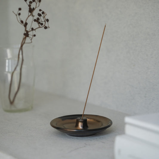 Gold and black Japanese incense holder with a lit stick on a light table, setting a serene mood for morning meditation.