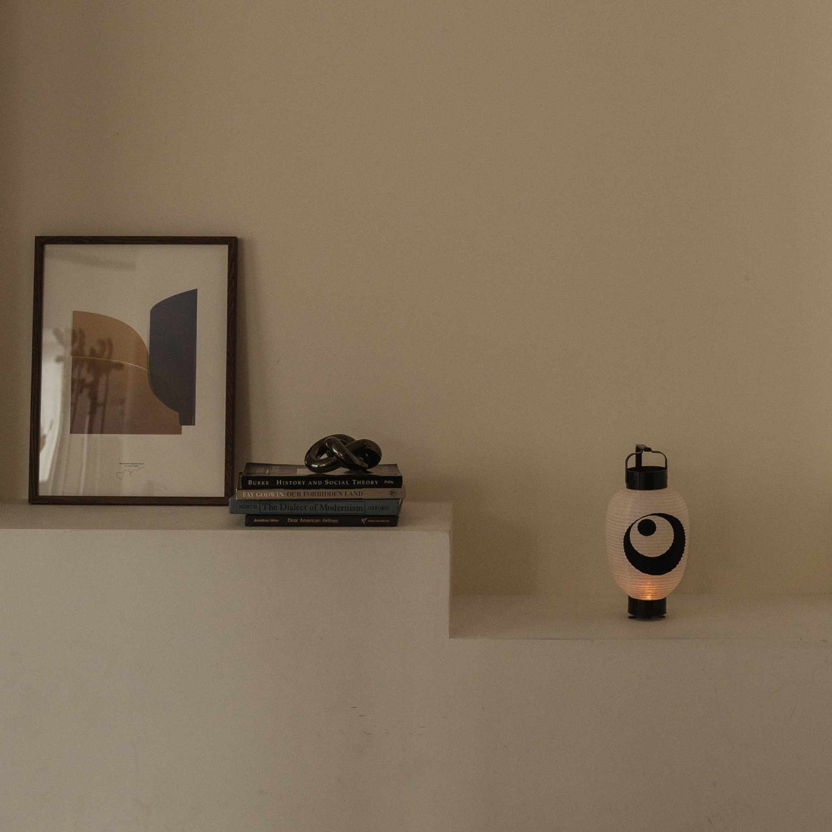 Standing Japanese lantern with moon and star motif placed on a white shelf next to books and art frame.