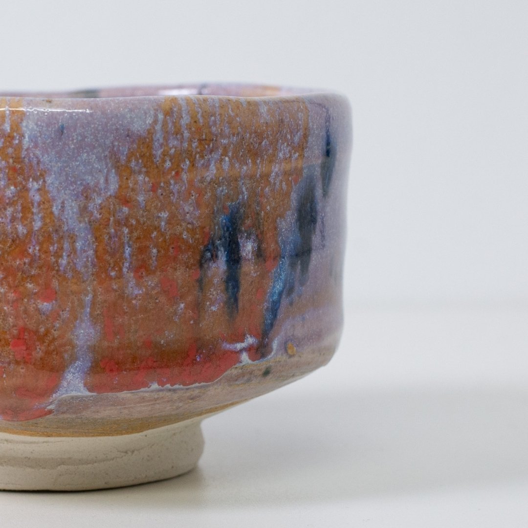 Close-up detail of "Navy & Red Splash" matcha bowl showing the artistic Kinyo glaze texture with red and navy blue drips over a pale purple base.