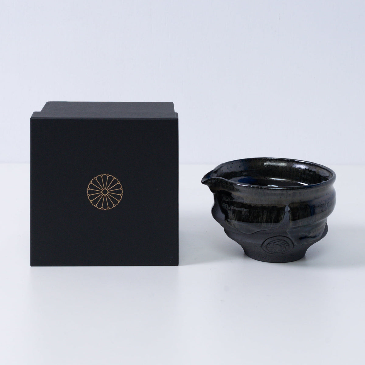 Japanse matcha kom met tuit "Dignity Blue" aardewerk naast een zwarte geschenkdoos met een gouden chrysant-embleem, uit Japan.