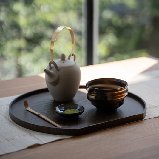 Japanese matcha bowl with spout and tea tools arranged on a dark tray by a sunny window for a peaceful authentic tea time.