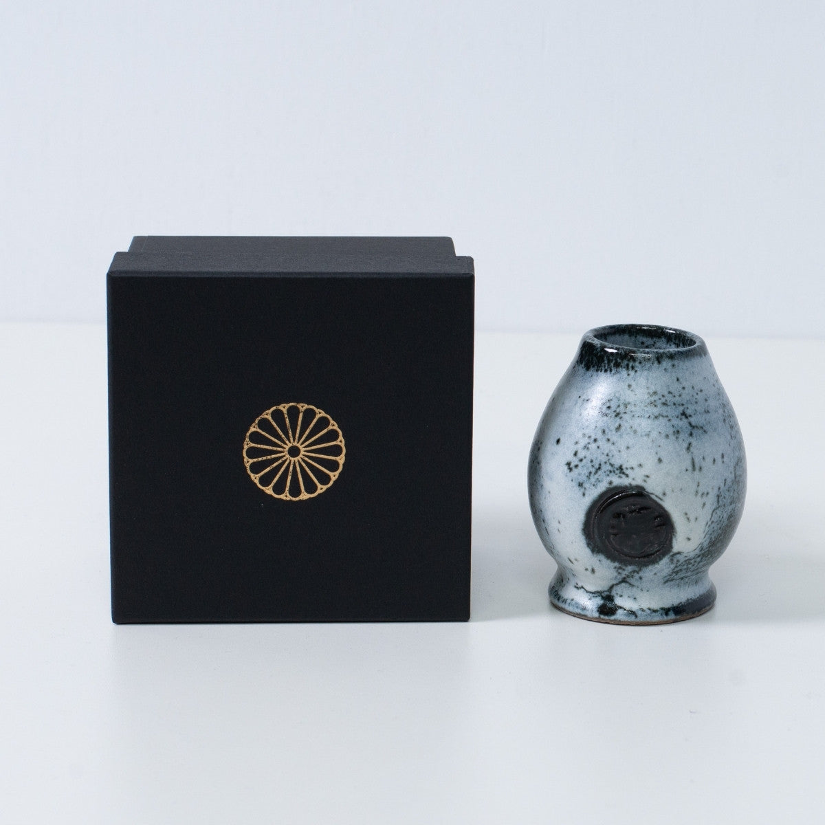 Wit en zwart Japans matcha garde-standaard "Creative Cloud" aardewerk naast een zwarte geschenkdoos met een gouden chrysant-embleem, uit Japan.