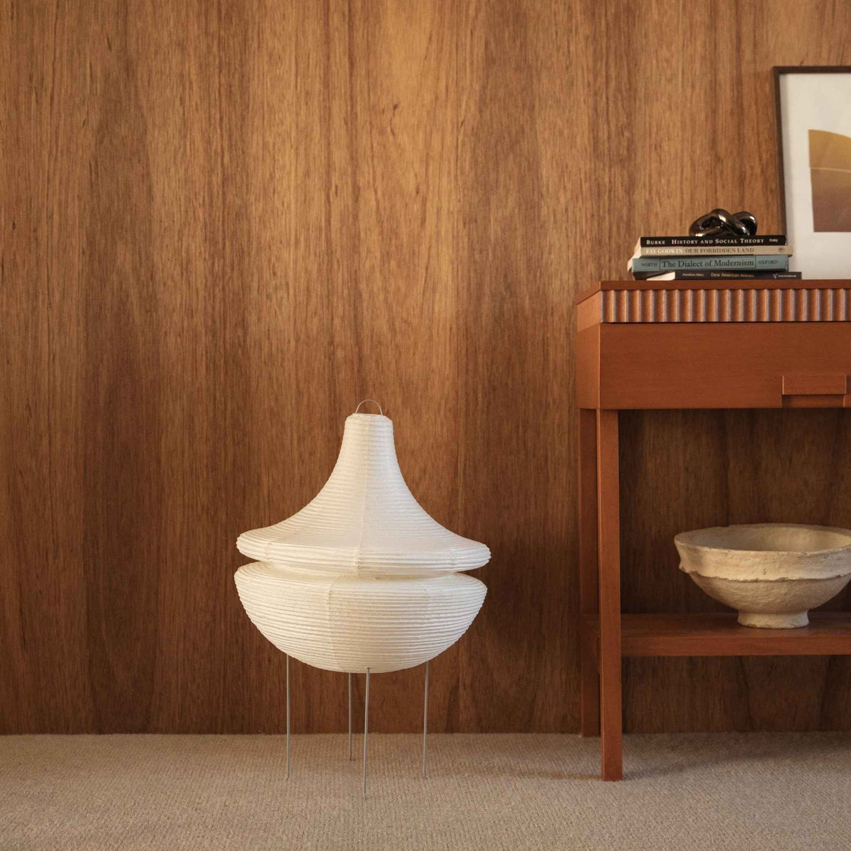 Onverlichte Japanse papieren vloerlamp Gemini 02 staand op een vloerbedekking naast een houten console tafel tegen een donkere muur