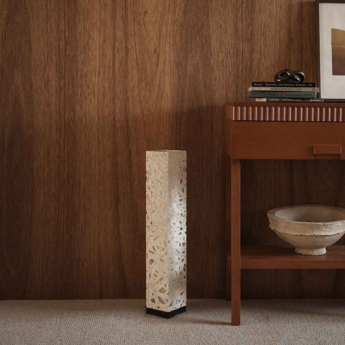 "Witte Me Look 02 papieren staande lamp onverlicht op een tapijt tegen een houten muur bij een console tafel."