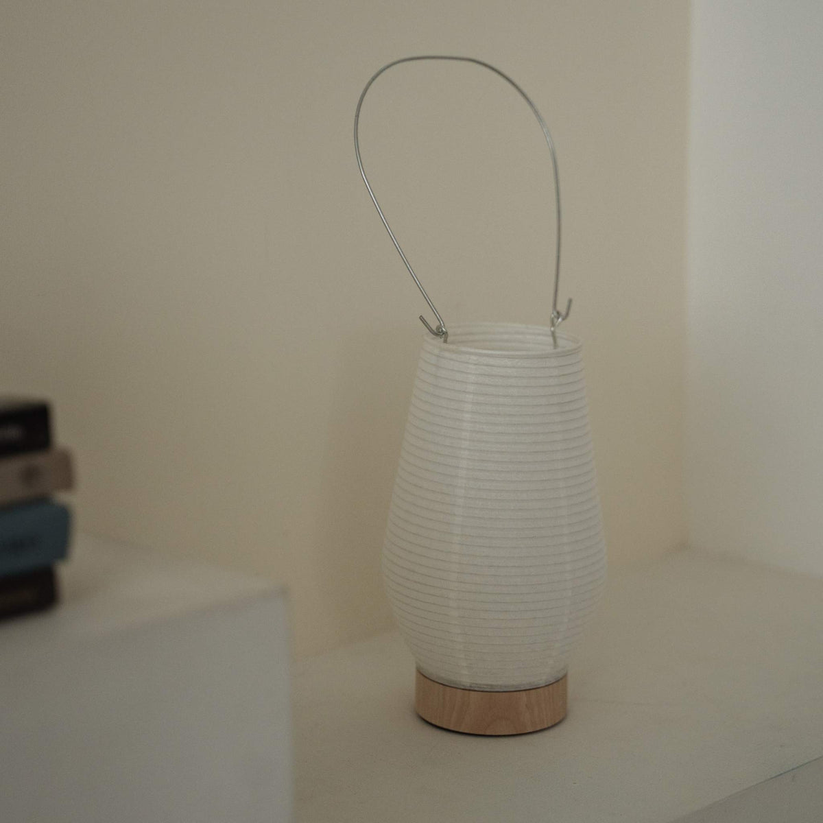A portable japanese paper lamp RIN 02 with a metal handle sitting on a white surface showing its delicate mino washi texture