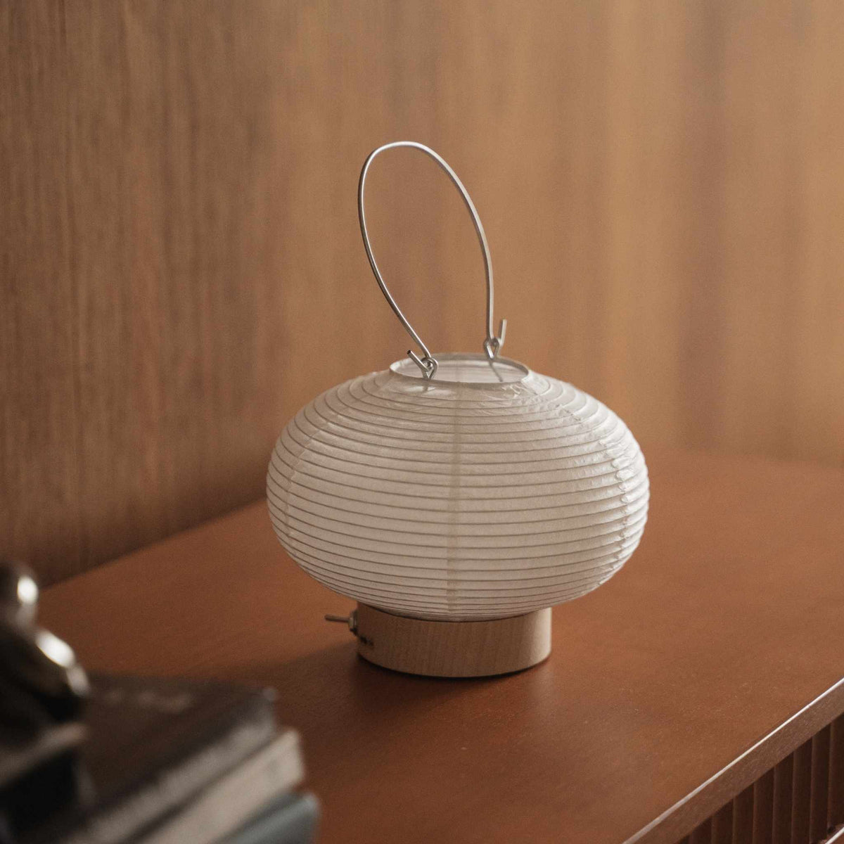 Lille japansk papir bordlampe Rin 03 stående på et brunt konsolbord i træ, der viser dens runde hvide form
