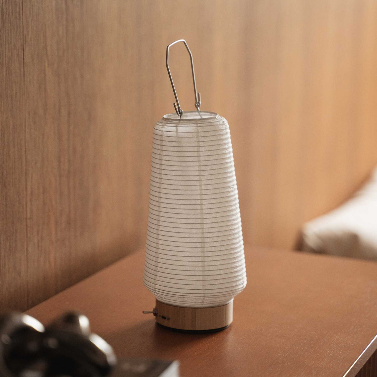 Small japanese paper table lamp Rin 04 sitting on a brown wooden console table showcasing its round white shape