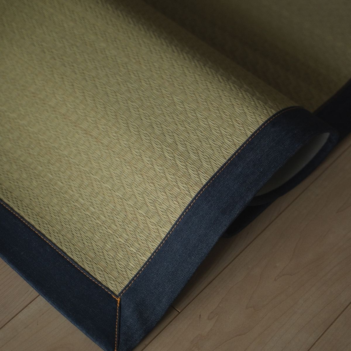 Japanse denim vloerkleed met tatami-structuur, opgevouwen op een houten vloer, voegt een stijlvol indigo accent toe aan modern Japans interieur.