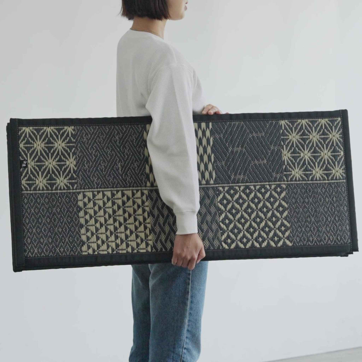 Woman carrying a folded black tatami mattress in a Japanese house demonstrating its lightweight design.