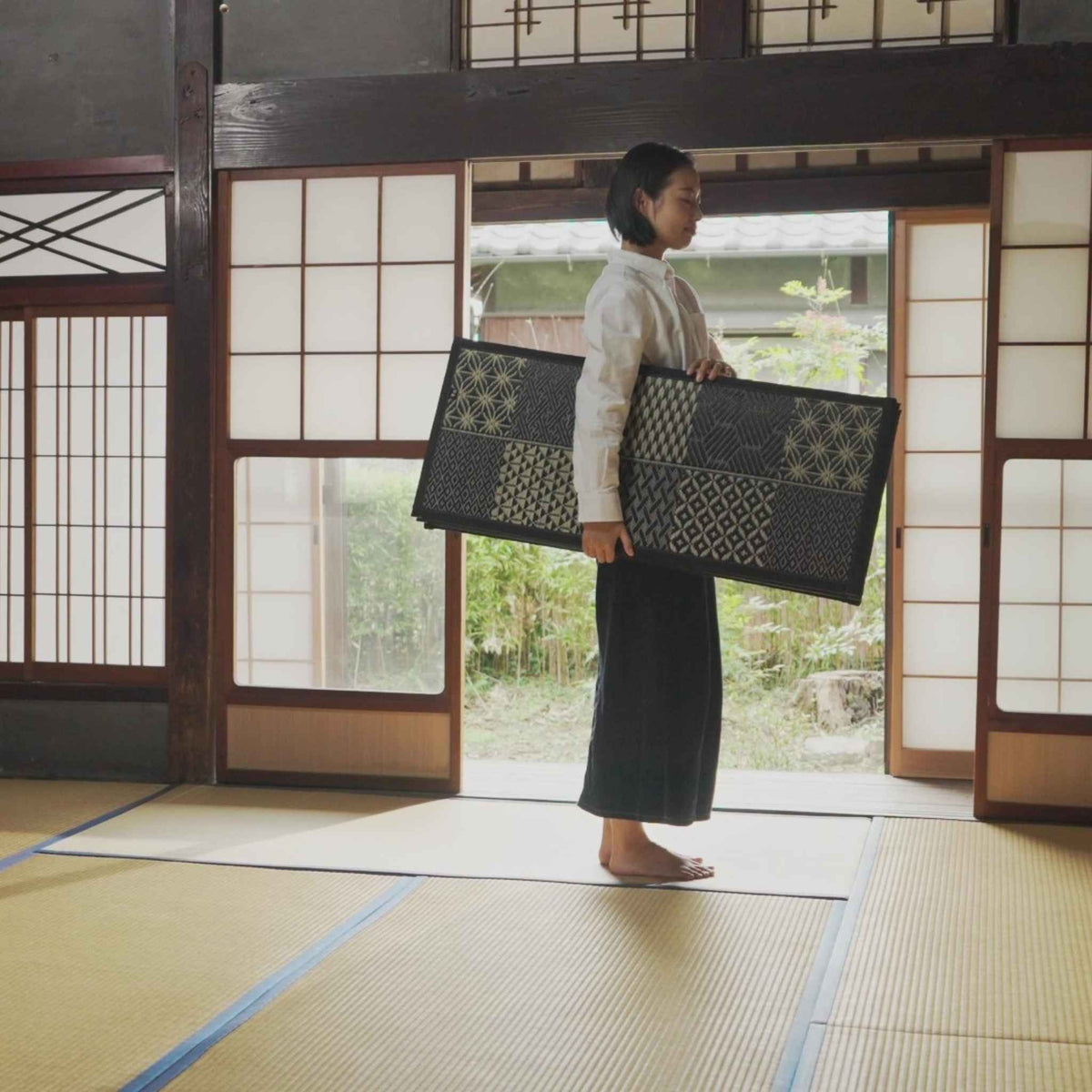 Woman carrying a folded black tatami mattress in a japanese house demonstrating its lightweight design.