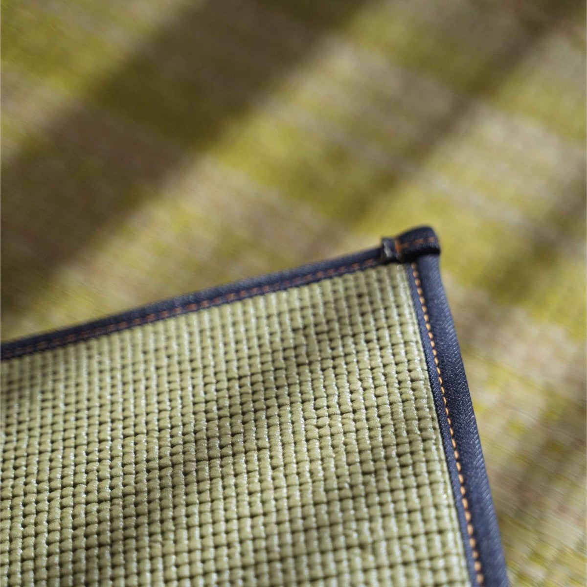 Close up of the non slip backing and denim hem on a green tatami yoga mat ensuring stability for exercise.