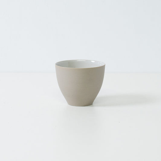 Side view of a single modern f shape japanese tea cup showing its curved unglazed white exterior and stable base