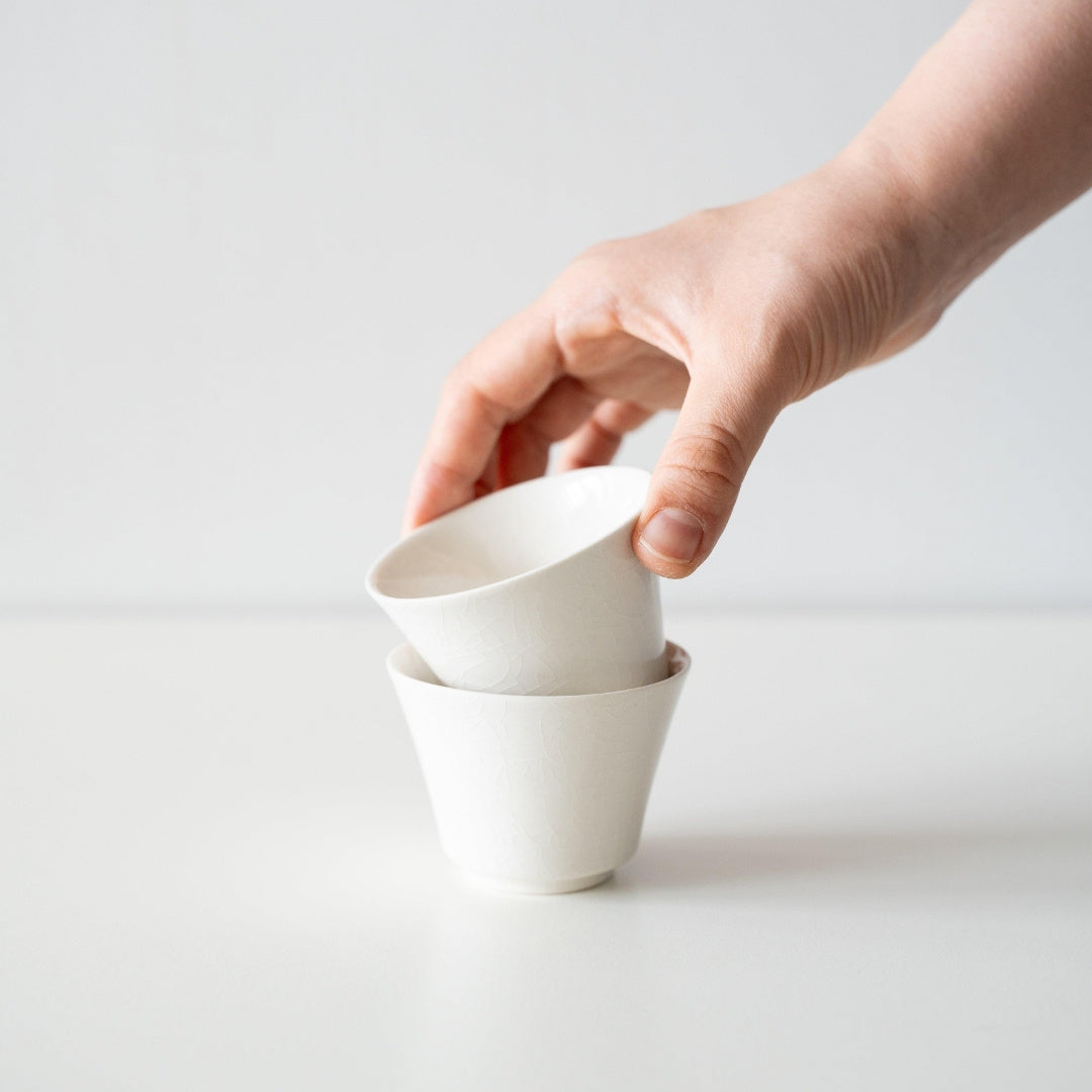 A hand stacking two white Japanese tea cups showing the high-footed design and the unique Kannyu crackle glaze texture.