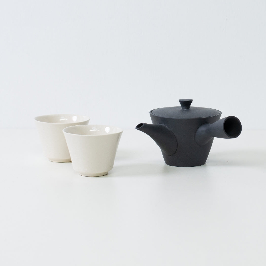 Japanse theeset met een zwarte kyusu theepot naast twee witte theekopjes met crackleglazuur voor gastvrijheid.