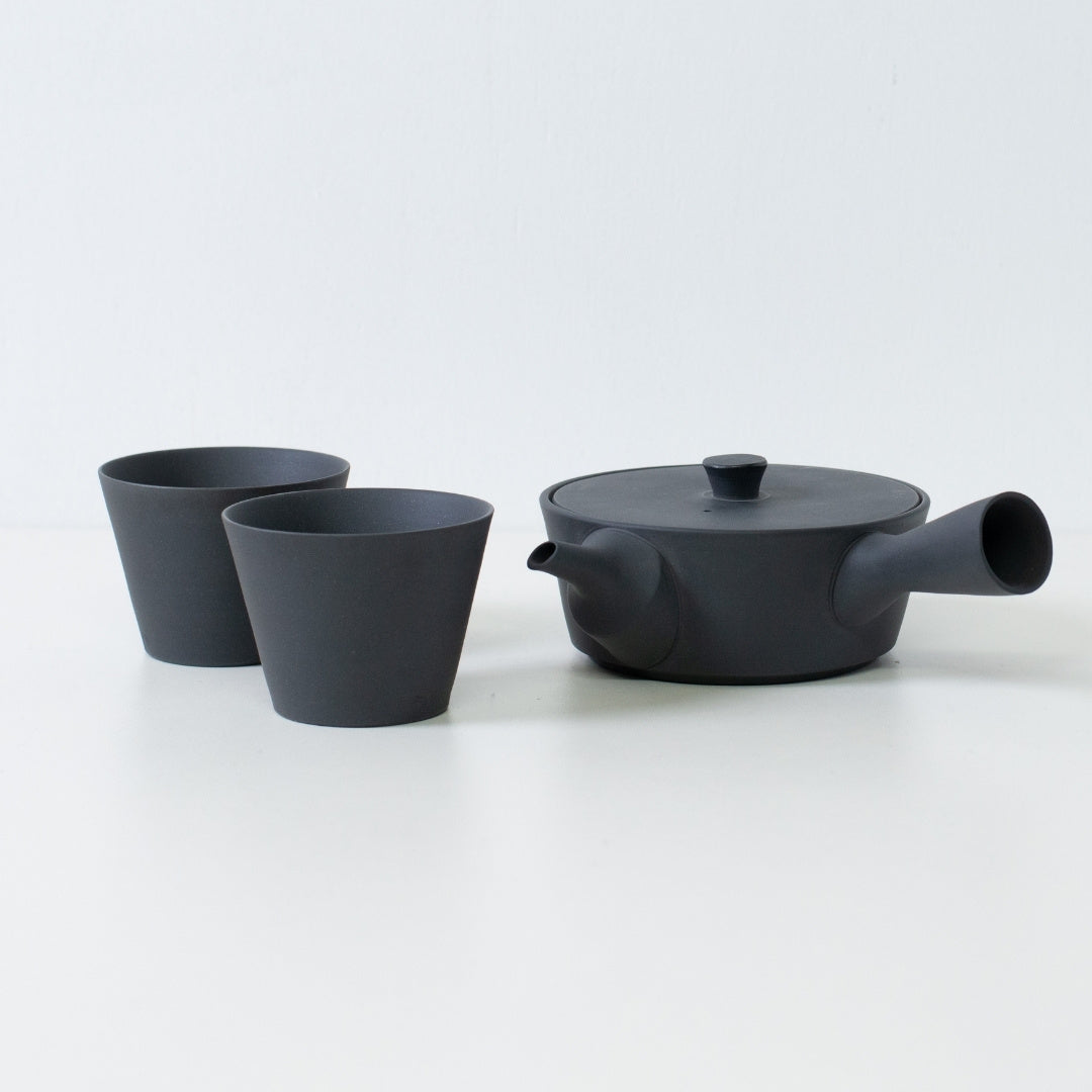 Modern black japanese tea set with a flat sencha kyusu teapot and cone shaped tea cups on a white table