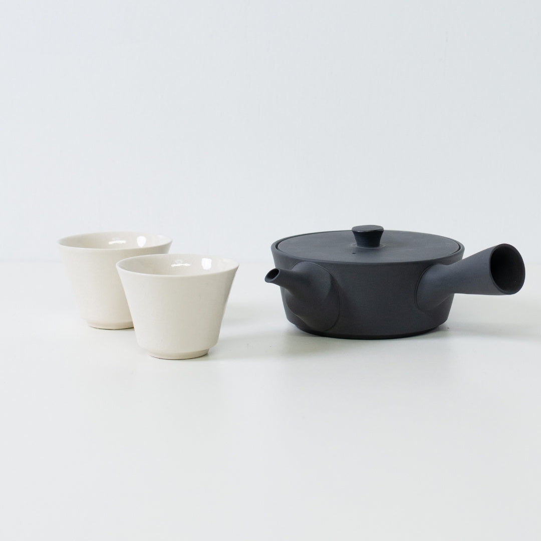 Flat black japanese teapot paired with glossy white high footed tea cups showing a contrast in texture.