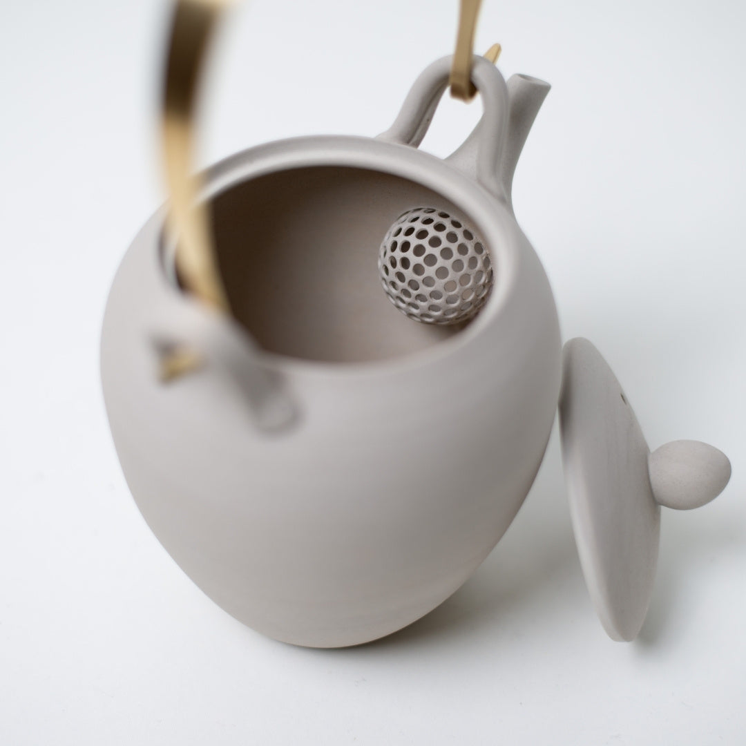 Open japanese teapot revealing the built in ceramic ball strainer inside the unglazed white clay kyusu body